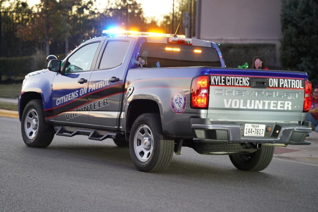 Pictures of the Kyle Citizens on Patrol volunteer vehicle. A large silver truck with a blue-painted front, red accents and flashing lights. Members of the Kyle Citizens on Patrol are in the vehicle, getting ready to take off for Santa Rides through Kyle.