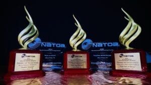 Three NATOA 2026 Government Programming Awards trophies with gold flame-shaped finials, each on a wood-tone base with engraved award details for the City of Kyle Communications Department.